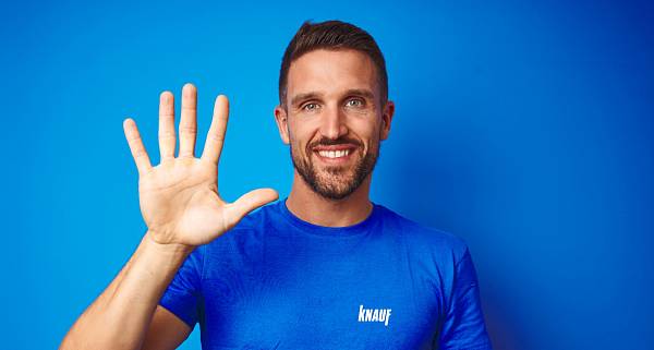 Fröhlicher Mann in einem blauen T-Shirt mit weißem Knauf-Logo der die Hand mit fünf ausgestreckten Fingern hochhält.