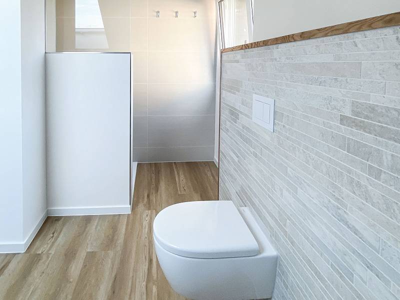 Blick in ein fertiges, modernes Badezimmer mit bodengleicher Dusche, Wand-WC und Designboden in Holzoptik.