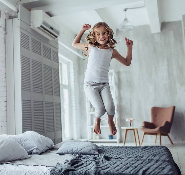 Fröhliches Mädchen hüpft auf einem Bett; im Hintergrund eine Balkendecke